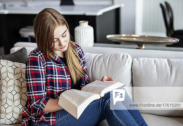 Teenage girl sitting on a couch at home and reading the Bible; Edmonton  Alberta  Canada