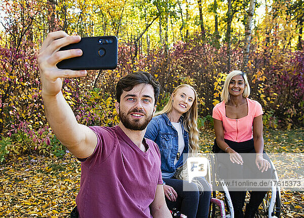Young paraplegic man and women in their wheelchairs taking a self portrait with a smart phone in a park on a beautiful fall day; Edmonton  Alberta  Canada