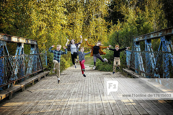 Fünf Geschwister in einer Reihe springen in der Luft und machen lustige Gesten auf einer Parkbrücke; Edmonton  Alberta  Kanada