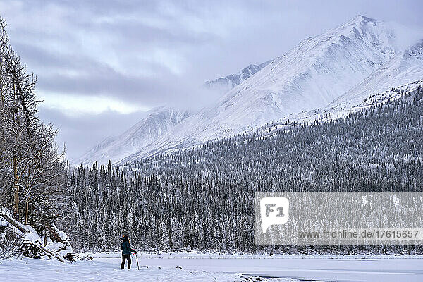 Frau steht am gefrorenen Ufer des Kathleen Lake und blickt auf die schneebedeckte Landschaft; Haines Junction  Yukon  Kanada