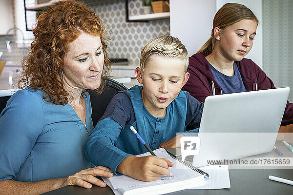 Eine Mutter mit ihrer Tochter im Teenageralter und ihrem kleinen Sohn sitzen zu Hause am Küchentisch mit einem Laptop und einem Tablet und machen Schularbeiten  während sie zu Hause unterrichtet werden; Alberta  Kanada