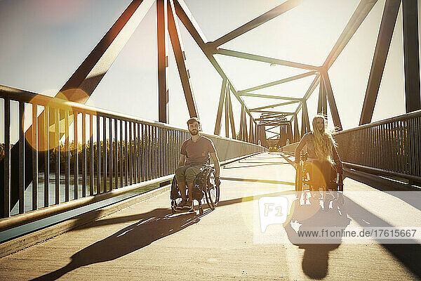Junger querschnittsgelähmter Mann und Frau  die an einem schönen Herbsttag gemeinsam in ihren Rollstühlen über eine Brücke fahren; Edmonton  Alberta  Kanada