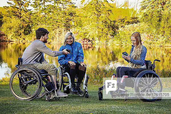 Group of three young paraplegics in their wheelchairs visiting together in a park on a beautiful fall day; Edmonton  Alberta  Canada