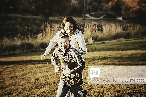 Mother chasing her son in a game of football on a beautiful autumn day in a city park; St. Alberta  Alberta  Canada