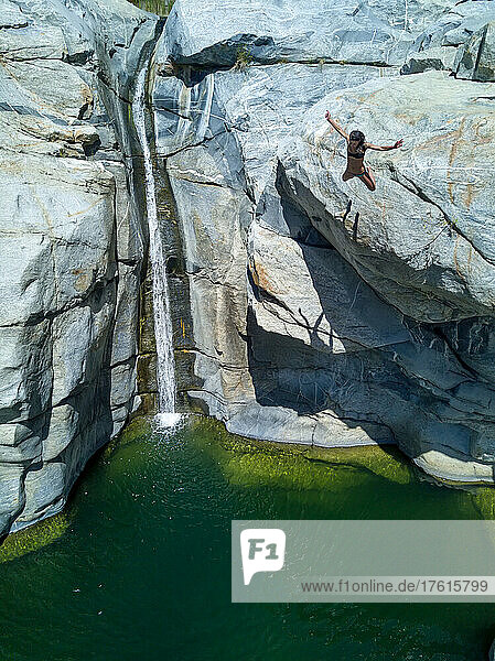 Eine Frau springt von einer Klippe in ein Wasserbecken.