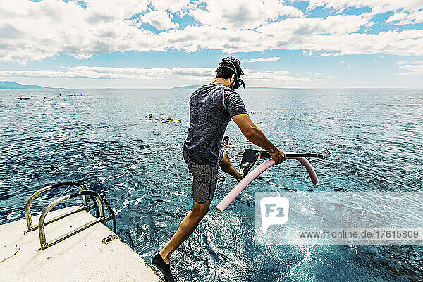 Mann  der mit Schnorchelausrüstung und einer Unterwasserkamera von einem Boot ins Wasser springt  um sich anderen Schnorchlern an der Küste von Maui anzuschließen; Maui  Hawaii  Vereinigte Staaten von Amerika