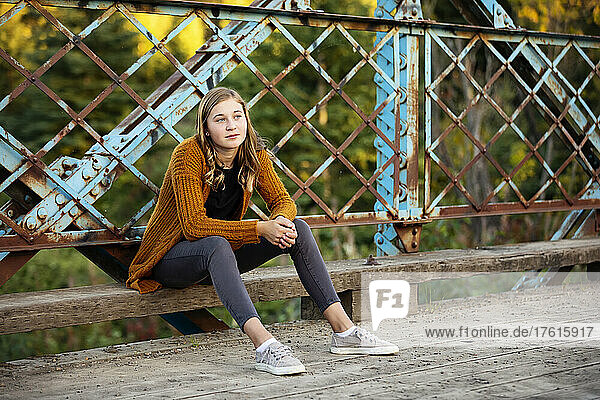 Teenage girl sits outdoors on a park bridge looking contemplative; Edmonton  Alberta  Canada