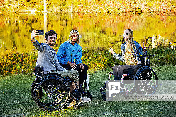 Young paraplegic man and women in their wheelchairs taking a self portrait with a smart phone in a park on a beautiful fall day; Edmonton  Alberta  Canada