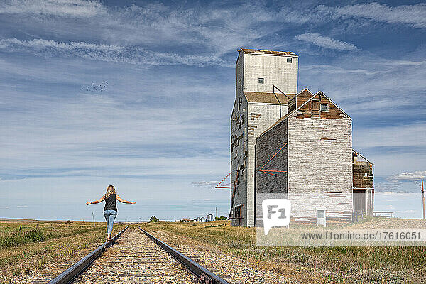 Woman walking on the railway tracks near an abandoned grain elevator in the ghost town of Sanctuary  Saskatchewan; Sanctuary  Saskatchewan  Canada