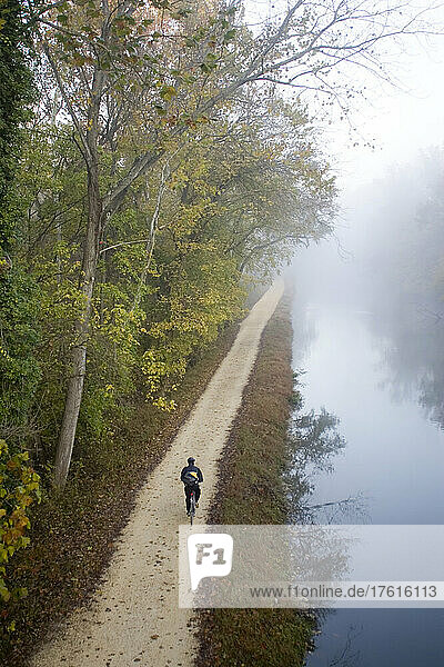 Fahrradfahrer  der im Morgennebel auf dem Treidelpfad zur Arbeit fährt; Chesapeake and Ohio Canal Towpath in der Nähe von Washington  District of Columbia.