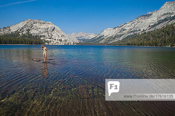 A young woman walks out into an alpine lake to cool off after climbing.