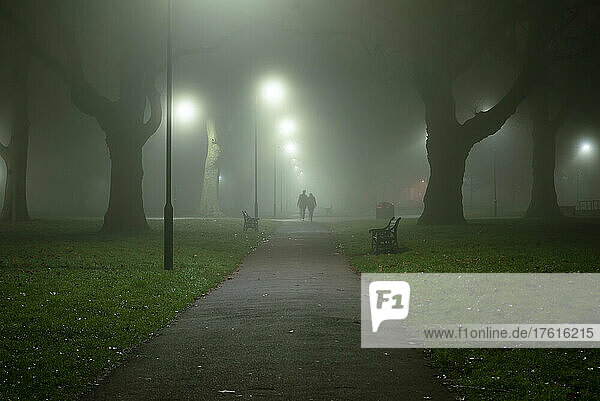 Silhouette von zwei Personen  die an einem nebligen Morgen in London Fields  Shoreditch  London  UK  spazieren gehen; London  England