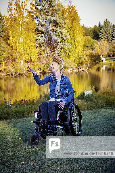Junge querschnittsgelähmte Frau in ihrem Rollstuhl in einem Park an einem schönen Herbsttag  sie fühlt sich sorglos  ihr langes Haar weht nach oben; Edmonton  Alberta  Kanada