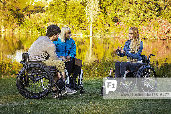 Group of three young paraplegics in their wheelchairs visiting together in a park on a beautiful fall day; Edmonton  Alberta  Canada