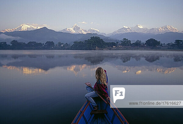Eine Frau in einem Ruderboot blickt in der Morgendämmerung auf die Annapurna-Kette; Annapurna-Kette  Himalaya-Gebirge  Nepal.