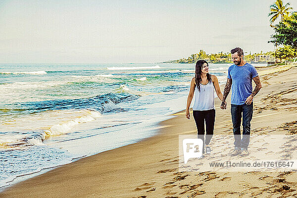 A couple walking down Ka'anapali Beach holding hands and talking together; Ka'anapali  Maui  Hawaii  United States of America