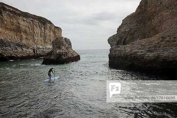 A stand up paddleboarder off the rough coastline north of Santa Cruz.