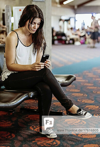 A woman sits in an airport waiting area using her smart phone; Kahului  Maui  Hawaii  United States of America