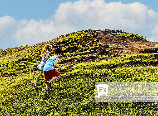 Zwei kleine Kinder klettern gemeinsam auf einen grasbewachsenen Hügel am Nakalele Point; Maui  Hawaii  Vereinigte Staaten von Amerika