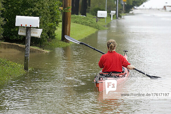 A woman paddles a sea kayak down the middle of a flooded road.; Cabin John  Maryland.