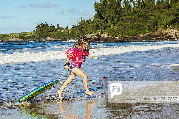 A young girl brings her bodyboard to shore at D. T. Fleming Beach after riding a wave; Kapalua  Maui  Hawaii  United States of America