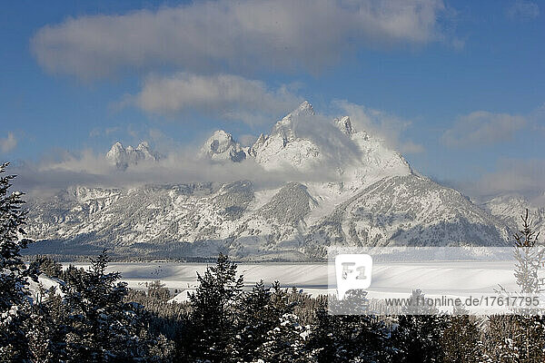 Snow covered Grand Tetons in Grand Teton National Park with a blue sky and low-lying clouds; Wyoming  United States of America