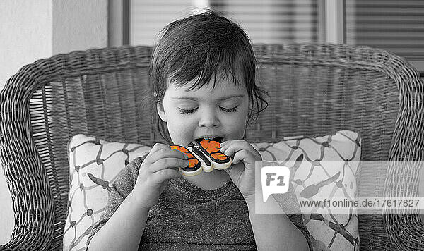 Junges Mädchen sitzt und isst einen Eiskeks in Form eines Schmetterlings  wobei nur der Schmetterling in Farbe ist; Surrey  British Columbia  Kanada