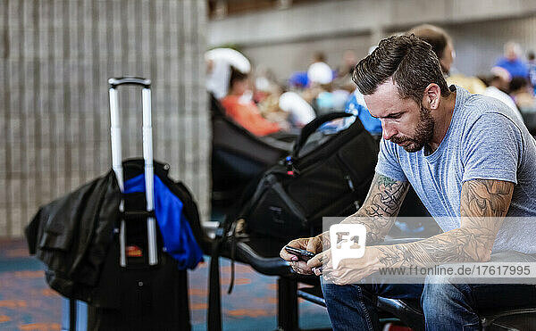 Ein Mann sitzt in einem Wartebereich eines Flughafens und benutzt sein Smartphone; Kahului  Maui  Hawaii  Vereinigte Staaten von Amerika