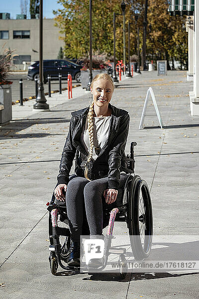Junge querschnittsgelähmte Frau in ihrem Rollstuhl auf einem städtischen Gehweg an einem schönen Herbsttag; Edmonton  Alberta  Kanada