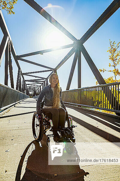 Eine junge querschnittsgelähmte Frau  die an einem schönen Herbsttag in ihrem Rollstuhl über eine Brücke fährt; Edmonton  Alberta  Kanada