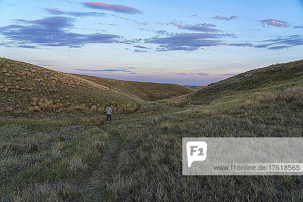 Frau auf einem Wanderweg im Grasslands National Park  Saskatchewan. Das späte Tageslicht beginnt den Himmel zu erhellen; Val Marie  Saskatchewan  Kanada