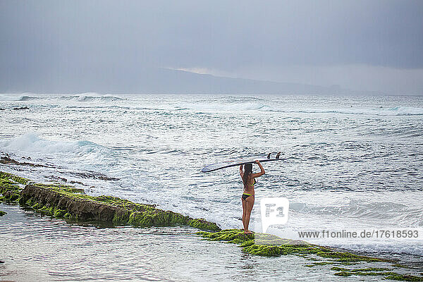 Eine Profi-Surferin trägt ihr Surfbrett auf die Wellen hinaus.