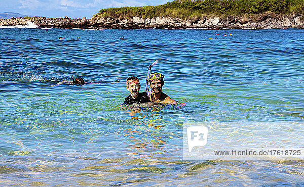 Ein Vater und sein kleiner Sohn im Meerwasser der Kapalua Bay mit Schnorchelausrüstung und posieren für die Kamera  während ein anderer Sohn im Hintergrund weiter schnorchelt; Kapalua  Maui  Hawaii  Vereinigte Staaten von Amerika