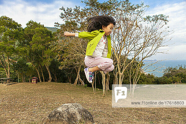 Junges Mädchen springt in der Luft über einen Felsen  wobei ihre langen Haare hinter ihr herfliegen; Hongkong  China