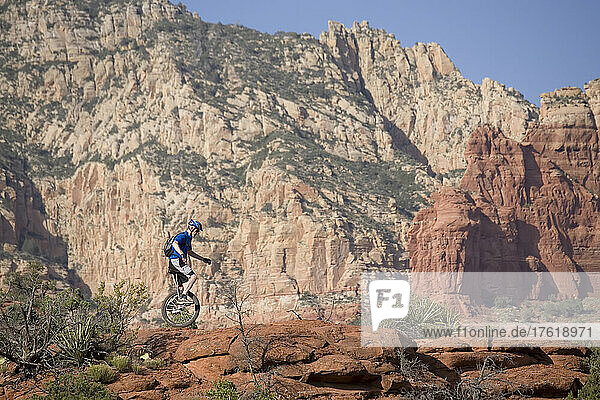 Ein Mann auf einem Einrad fährt entlang eines felsigen Bergrückens in der Wüste von Arizona; Sedona  Arizona.