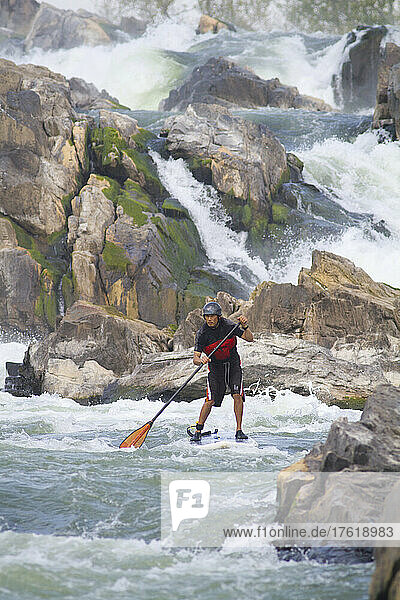 A stand up paddle boarder in white water just below Great Falls.; Potomac River  Maryland/Virginia.