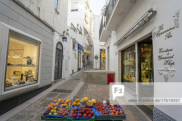 Fashion shops and a stall with fresh vegetables and fruit displayed in the narrow street in Capri; Capri  Naples  Italy
