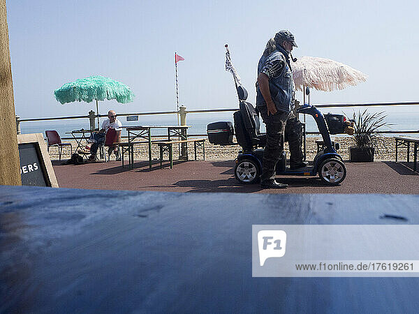 Man with pipe and cap about to ride a mobility scooter on seafront  Hastings  East Sussex  UK; Hastings  East Sussex  England