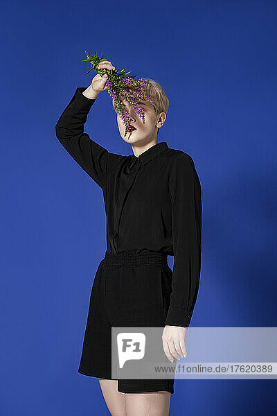 Fashionable woman covering face with flowers in studio