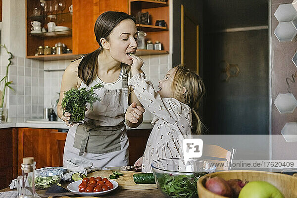 Girl feeding food to mother in kitchen at home