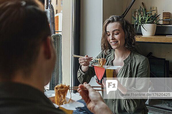 Smiling woman eating chinese food with boyfriend at home
