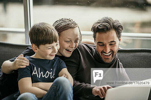 Happy man pointing on laptop sitting with sons at home