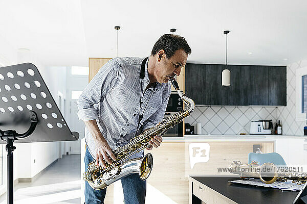 Musician playing saxophone in kitchen by table at home