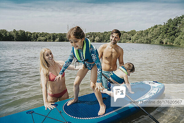Geschwister treiben zusammen mit ihren Eltern auf einem Paddleboard über den See