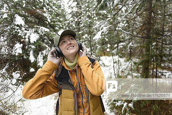 Smiling woman looking up listening music on headphones in winter forest
