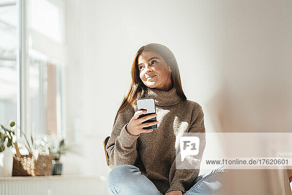 Contemplative woman with smart phone at home