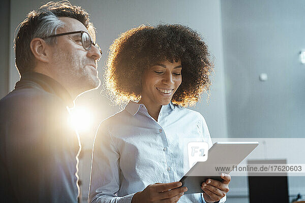 Smiling businesswoman discussing over tablet PC with colleague in office
