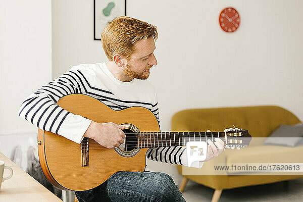 Junger Mann übt zu Hause im Wohnzimmer Gitarre