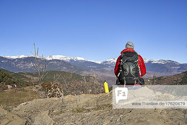 Wanderer mit Rucksack sitzt neben Wasserflasche auf Felsen