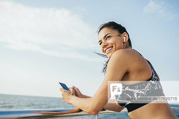 Happy beautiful woman with smart phone standing by railing